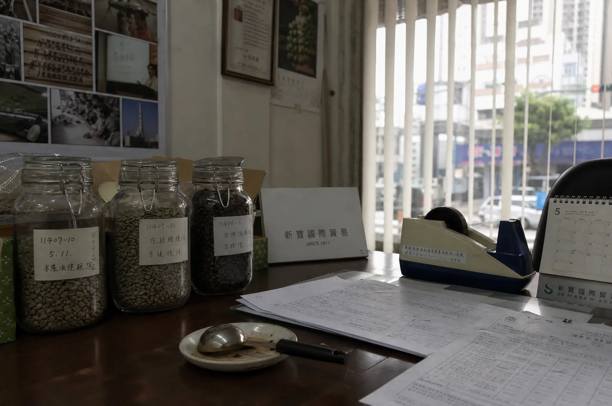 台灣辦公室一隅,樣品豆罐與杯測匙整齊排列,窗外是新莊的日常街景。